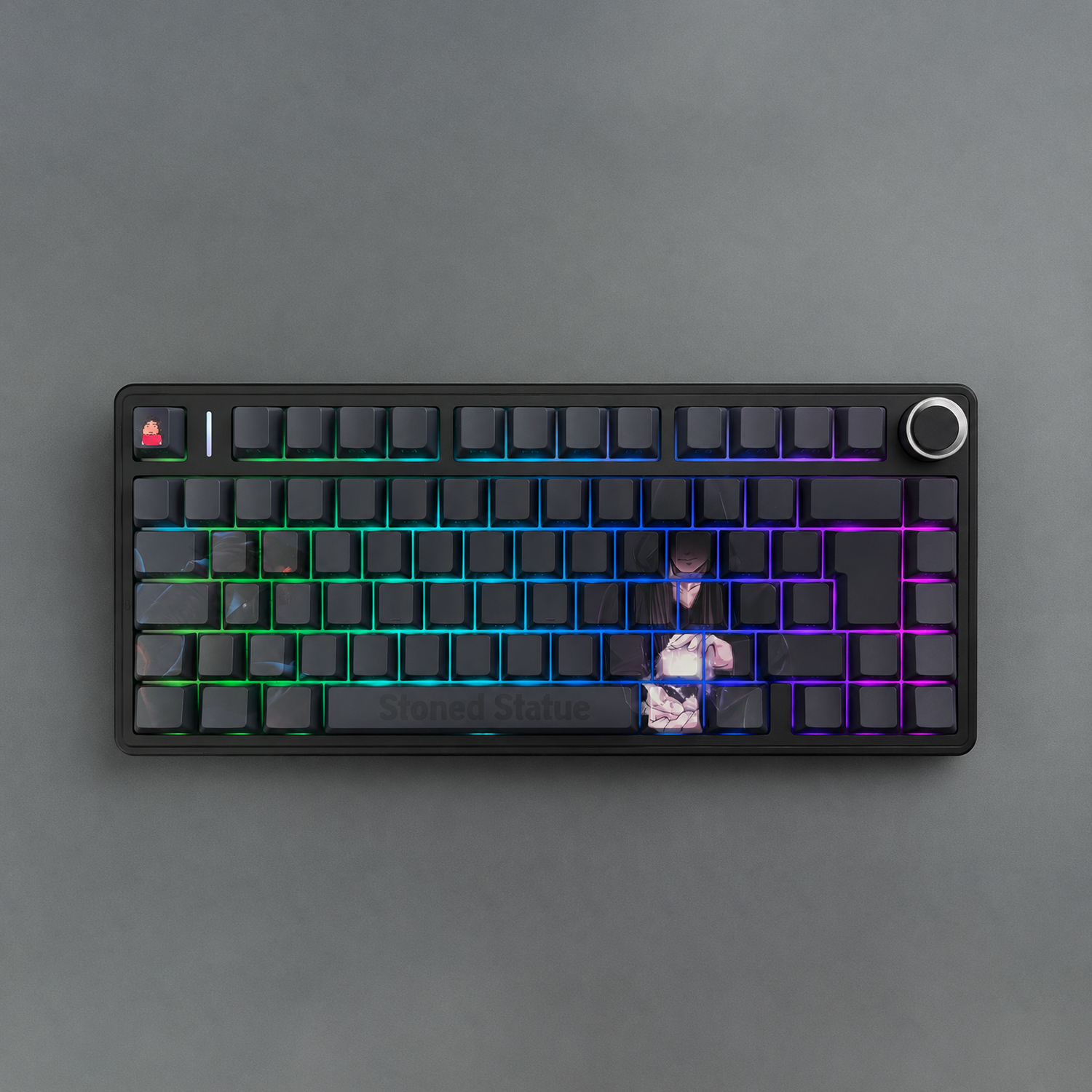 Vista superior de un teclado mecánico negro con iluminación RGB de arcoíris, una pequeña tecla de caracteres a la izquierda y un gran dial en la parte superior derecha.